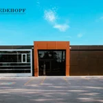 Front view of a commercial building with glass windows, a brown entrance, and a parking lot.