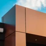 Corner of a modern commercial building with metallic brown panels and blue sky.