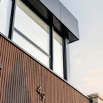 Close-up of black ACM panels and WPC siding near a garage door.