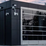 A vertical view of a commercial building's black facade with large windows and security cameras.