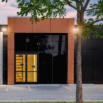 The front entrance of a modern commercial building with a tree in the foreground.