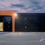 A wide view of a modern commercial building with black and metallic brown ACM panels and a parking lot.