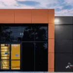 The front entrance of a modern commercial building with black and metallic brown ACM panels at sunset.