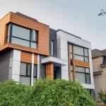 Modern home facade with green foreground bushes and mixed material siding blocks.