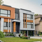 Angled view of a contemporary house with mixed siding, stone, and extensive landscaping.