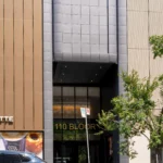 Wide street view of a multi-story commercial building with gray and brown aluminum panels.