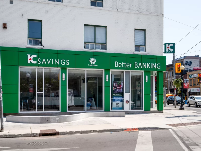 Green ACM commercial wall panel cladding on a bank facade with large glass storefront windows.