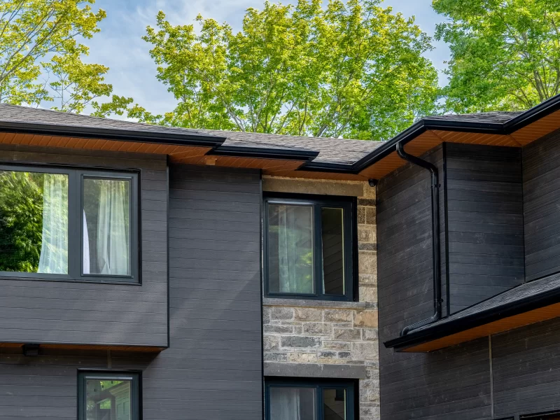 Detail of the upper facade showing dark anthracite cladding interspersed with light grey stone veneer walls and dark-framed windows.