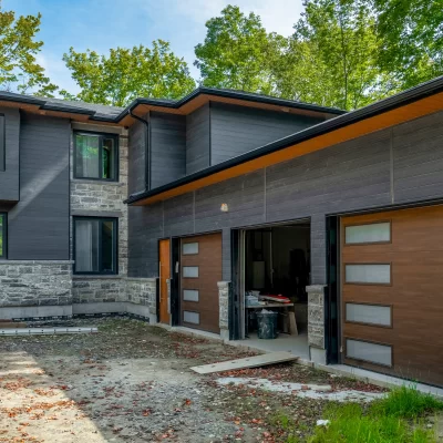 Expansive modern home with two garage bays featuring faux wood doors, stone veneer base, and dark anthracite cladding on the upper levels.