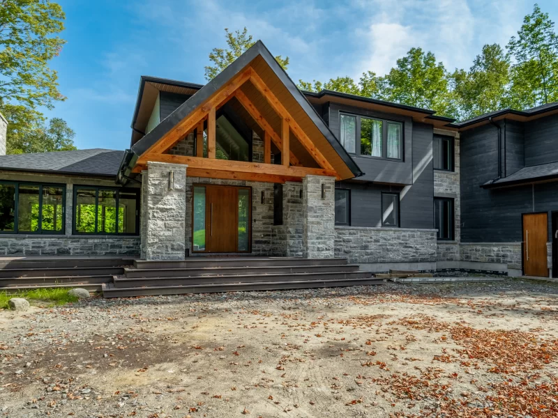 Grand modern home exterior featuring an A-frame entrance with exposed wood beams, grey stone veneer, and dark horizontal anthracite cladding.