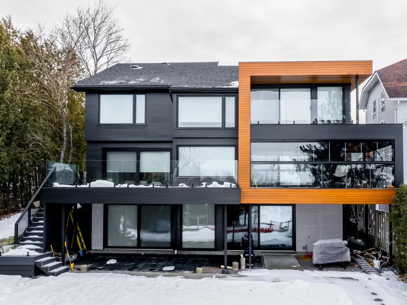 Large lakefront home with a two-tone facade using black anthracite composite cladding and vertical accents of wood-look cladding.