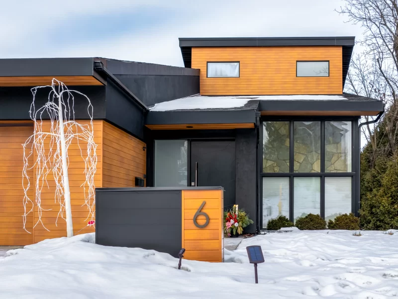 Modern home entrance in winter, featuring a two-tone facade of black and wood-look cladding and a prominent house number 6.