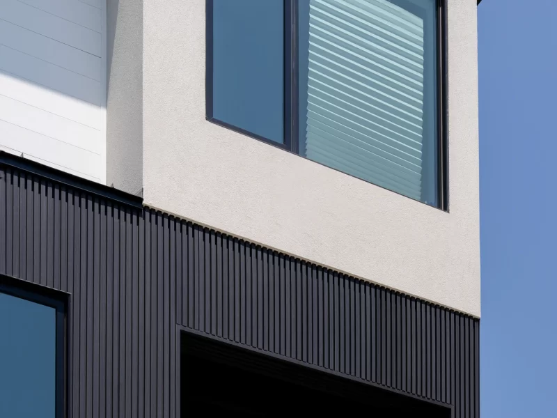 Corner detail of a modern facade showing the intersection of white stucco and dark vertical anthracite siding below a large window.