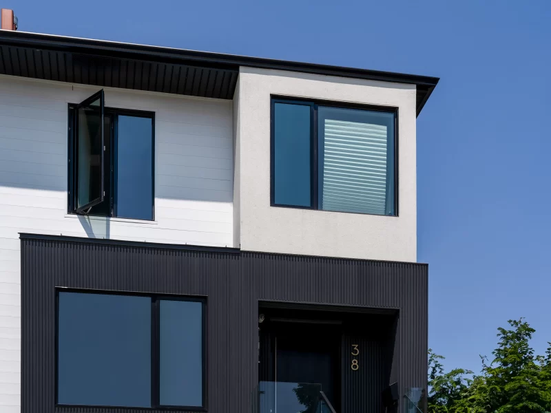 Detail of the upper facade: white horizontal siding, white stucco, and the transition to the lower section with dark anthracite siding.