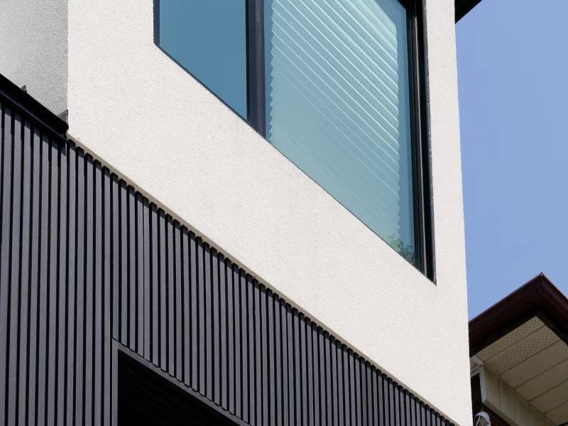 Upward view of a two-story residential facade with dark vertical anthracite siding on the lower level and white stucco above.