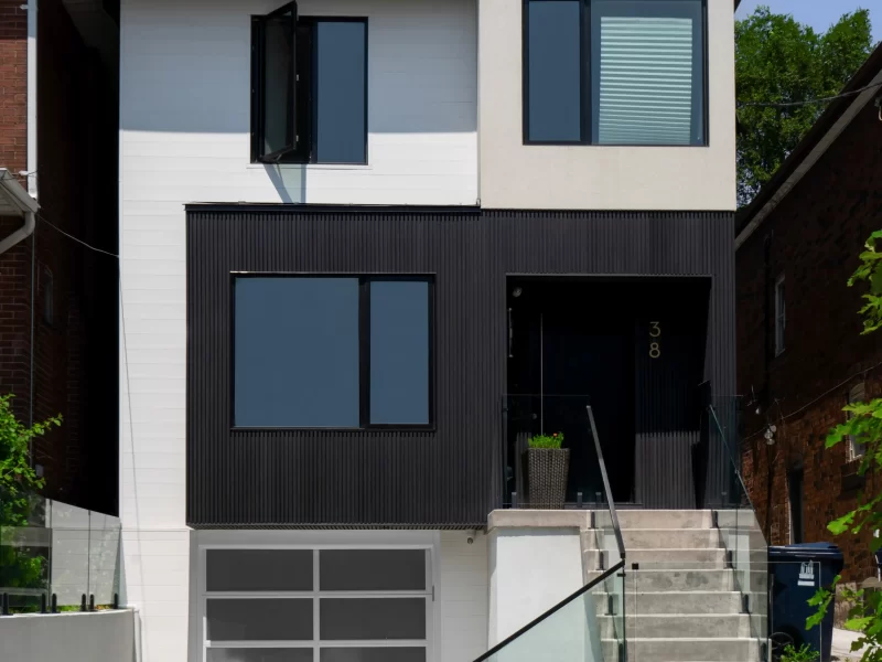 Full front view of a two-story modern house with a mix of white and anthracite siding, glass-paneled garage door, and stepped entrance.