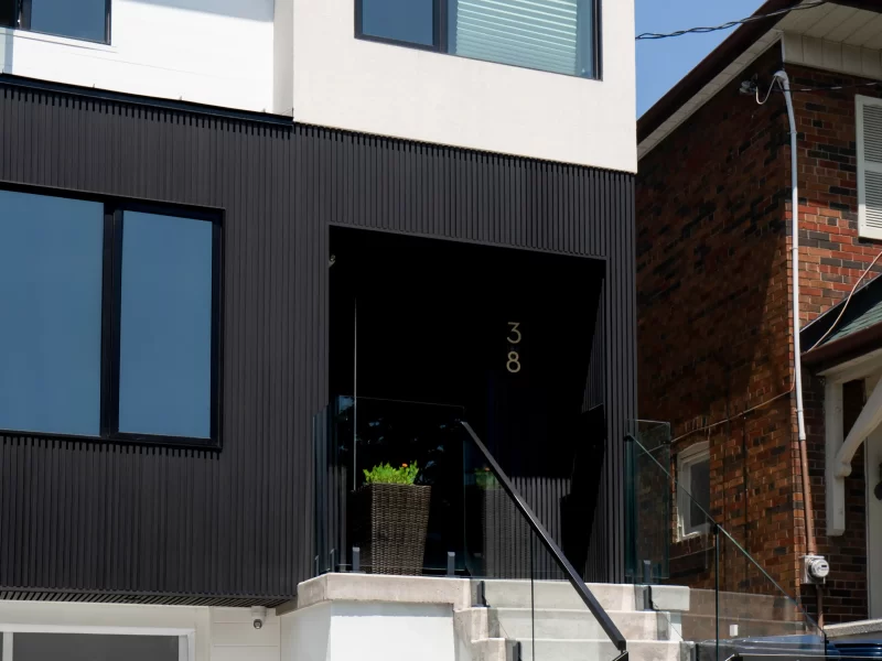 Front view of a multi-story home entrance featuring concrete steps, glass railing, and lower section covered in anthracite siding.