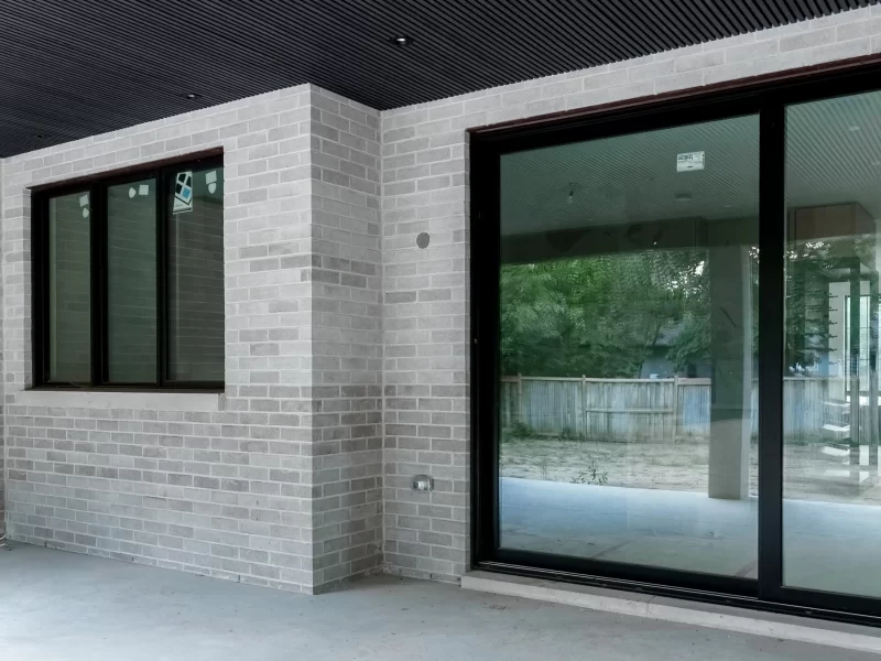 Modern exterior patio with gray brick, large glass sliding doors, and a linear black anthracite soffit ceiling with recessed lights.