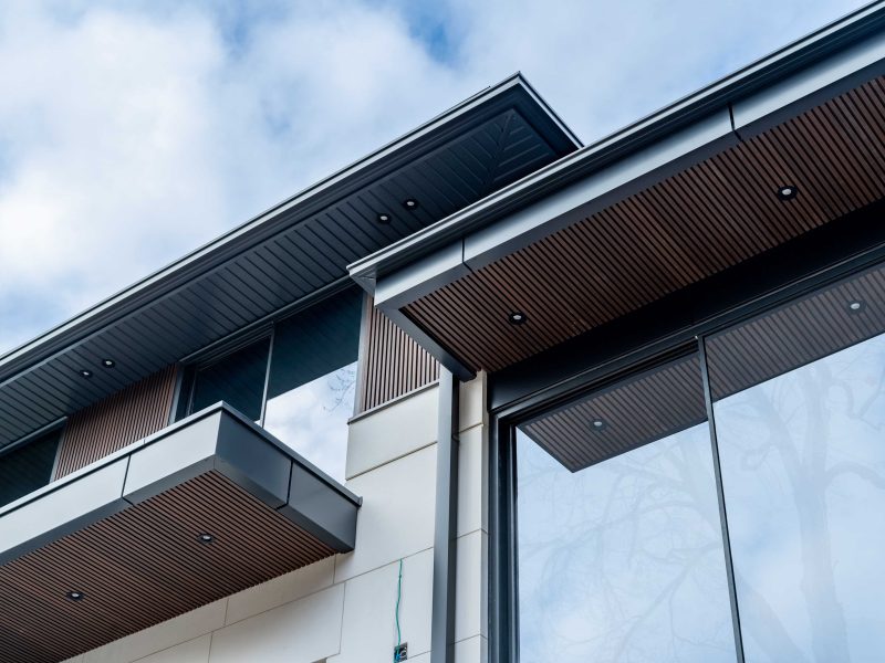 Exterior detail of a modern home showing fluted siding on the underside of overhangs and around large windows.