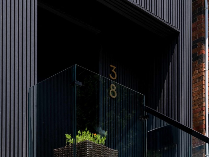 Close-up of a modern balcony featuring black vertical fluted siding, a glass railing, and a dark woven planter.