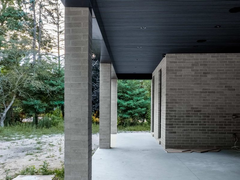 View from a concrete patio looking out, featuring a black fluted ceiling and light grey brick pillars.