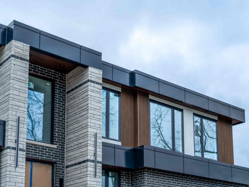 Exterior of a multi-story building featuring white stone, black brick, and vertical brown fluted siding accents.
