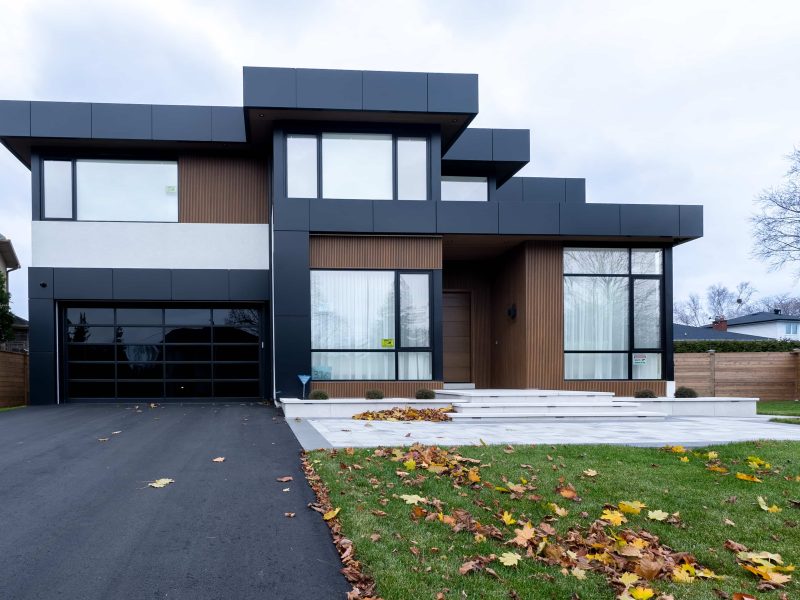 Modern two-story house with black panels, white stone, and vertical wood-look fluted siding under a cloudy sky.