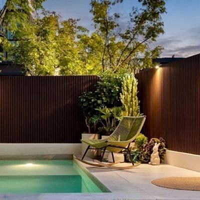 Dark brown WPC fluted fencing surrounding a modern backyard pool area with a green lounge chair and warm accent lighting.