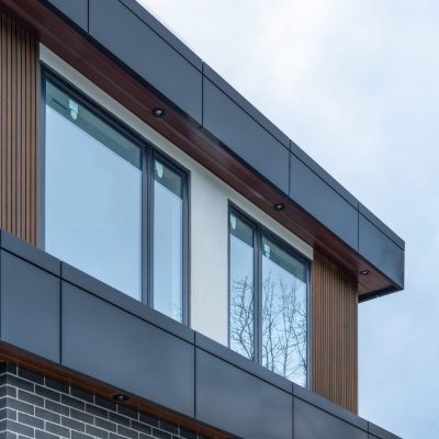 Modern building exterior featuring vertical wood-look fluted cladding, dark grey panels, and large glass windows.